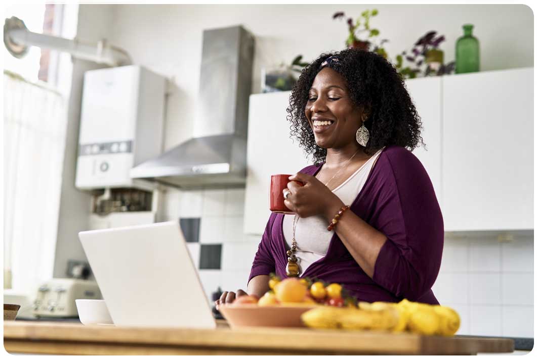 Smiling woman in kitchen looking at laptop
